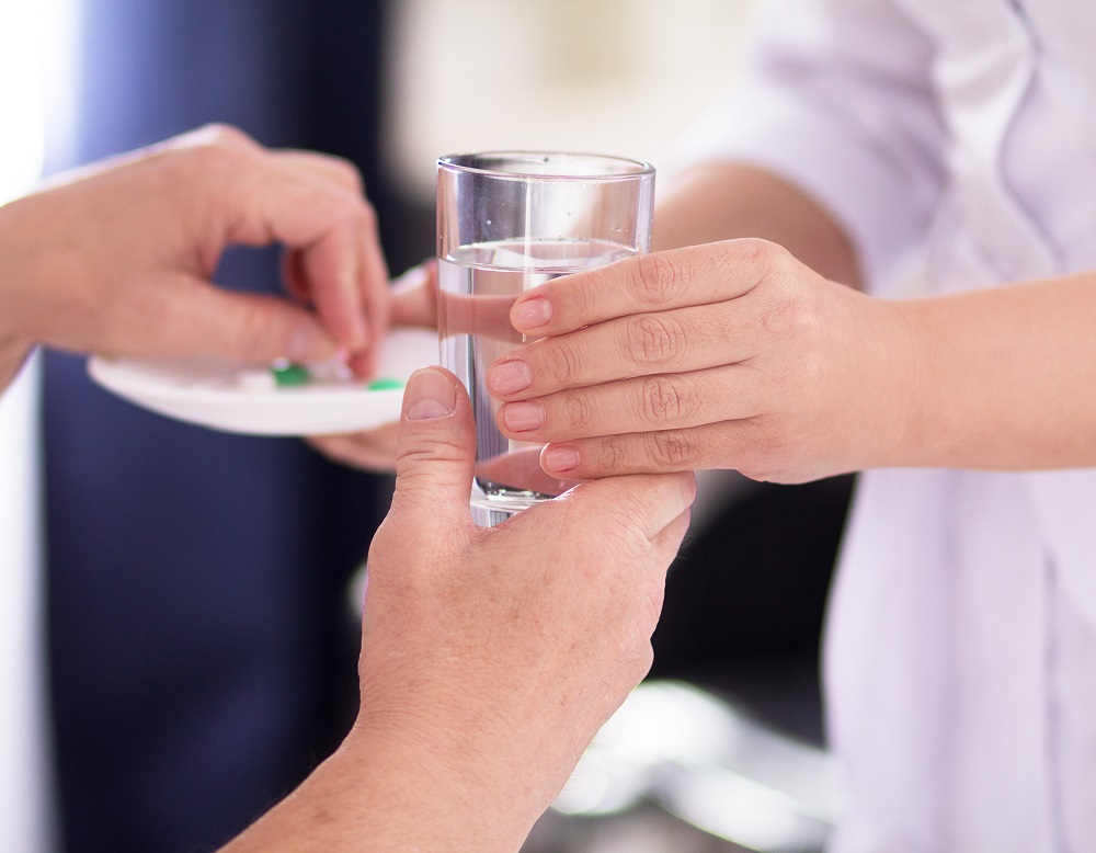 Infirmière donnant un verre d'eau et un médicament à un patient dans l'Hérault